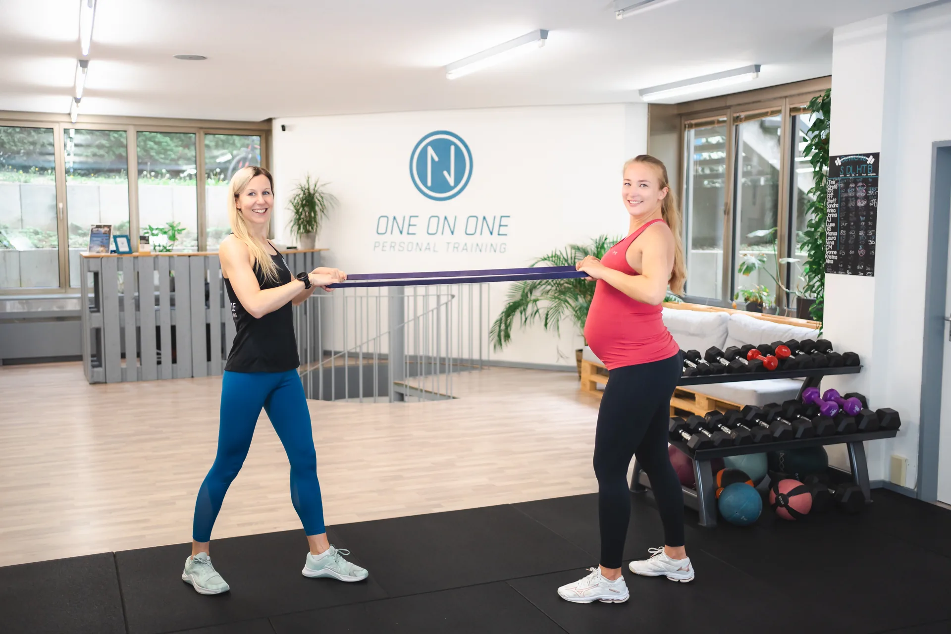 Trainerin begleitet eine Schwangere bei einer Kraftübung mit dem Trainingsband